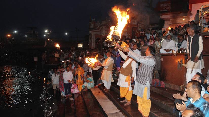 People performing Ganga aarti on the banks of a river with diyas.