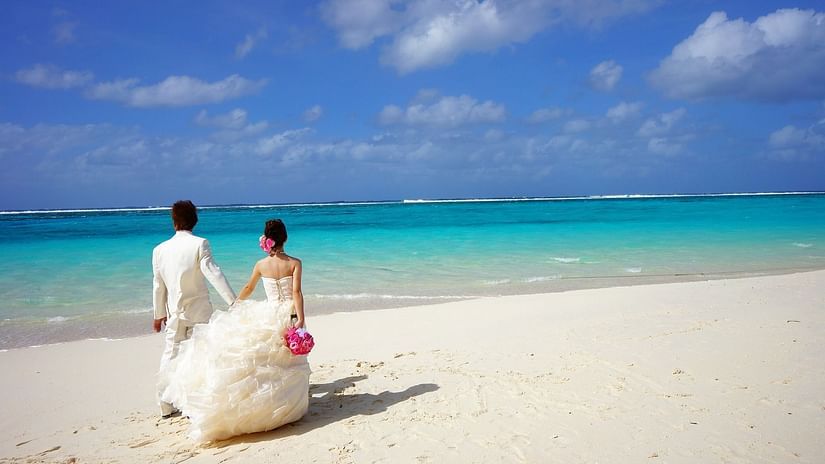 a bride and groom walking along beach posing for a picture with blue sky in the background