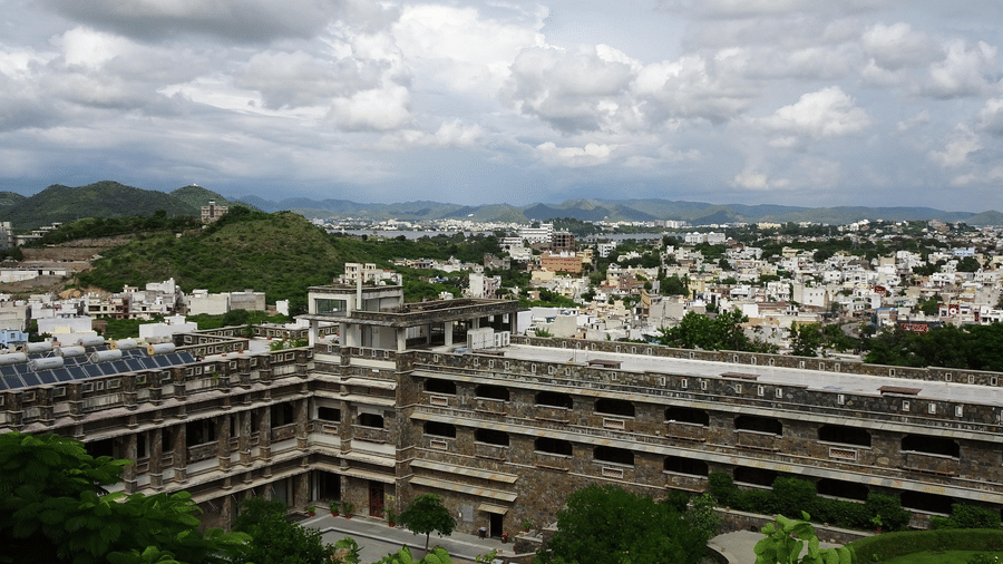 High-angle view of a large, modern stone building complex nestled amongst green hills and a sprawling city.