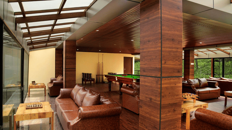 Shot of the indoor play area at the villa with brown sofas around Shot of the balcony at the villa with chairs kept | Ibex Stays and Trails, Valparai (Tale Rock)