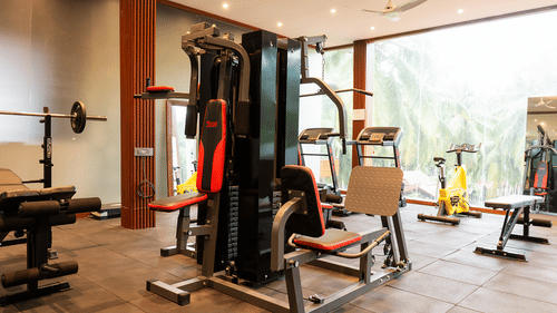 Interior view of a resort gymnasium with a multi-station machine, treadmills, and a bright view of tropical trees.