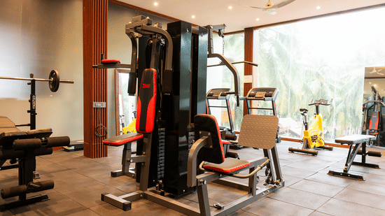 Interior view of a resort gymnasium with a multi-station machine, treadmills, and a bright view of tropical trees.