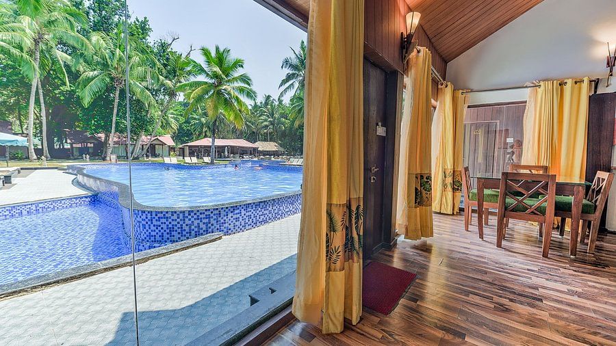 Bright and airy resort bedroom with direct access to a swimming pool through sliding glass doors, surrounded by lush greenery and equipped with wooden furniture and tropical decor.