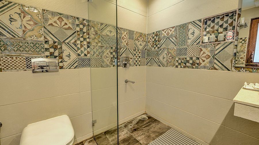 Elegant resort bathroom with decorative, multicolored patterned tiles on the walls, a modern glass shower, and white sanitary ware.