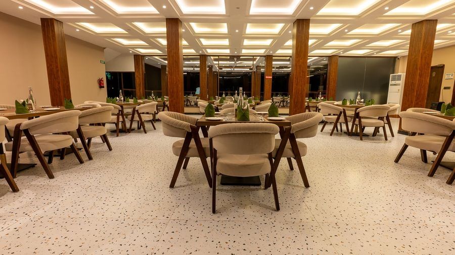 Elegant indoor dining area of a resort restaurant with modern chairs, set tables, and brightly lit ceiling panels.