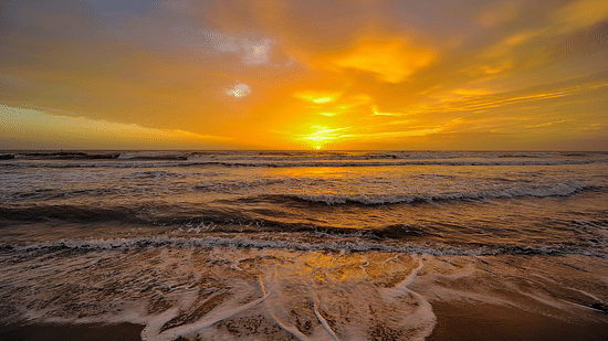 Beach waves at the shore with the sun setting in the background