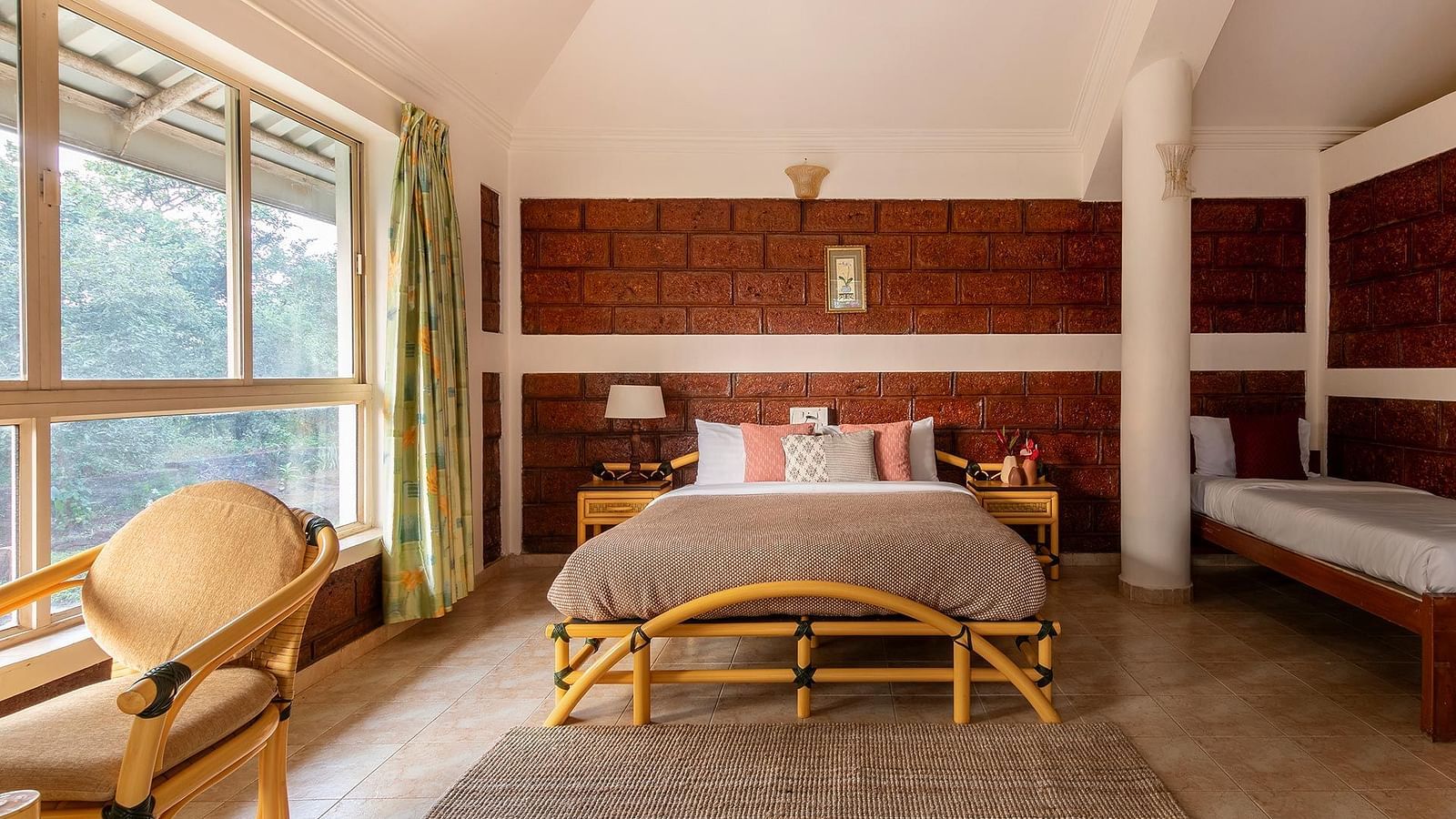 A double bed room with rug, glass windows with curtains, wooden floor, pillar, work chair and side tables