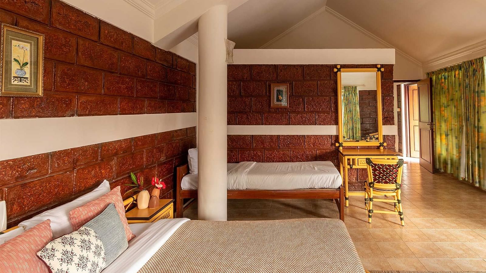 A double bed room, another single bed, a pillar, side table, wooden floor and a mirror