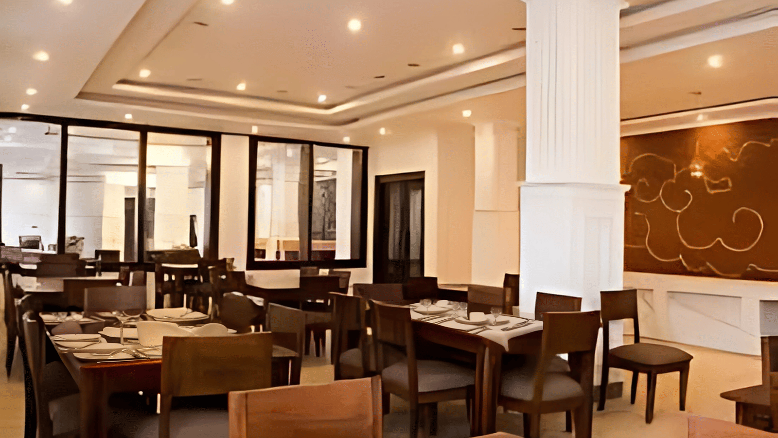 The spacious indoor restaurant at Hotel Dekiling by Eastlynn Collections, Leh, with wooden dining sets, pillars, and large glass windows.