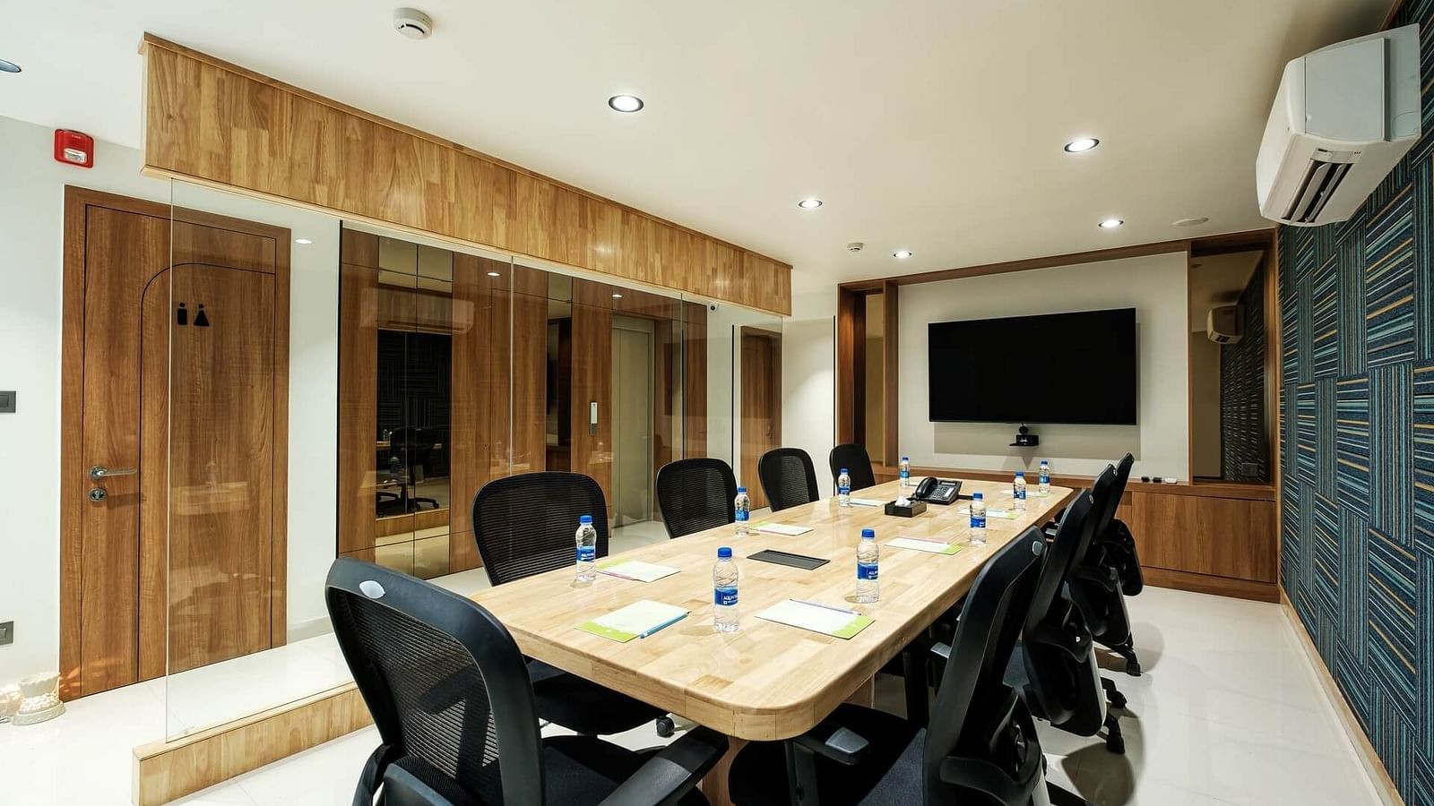Diagonal view of the full boardroom at Indie Stays, Jaipur, with chairs along the sides, a screen at the front, and a wall-mounted AC.