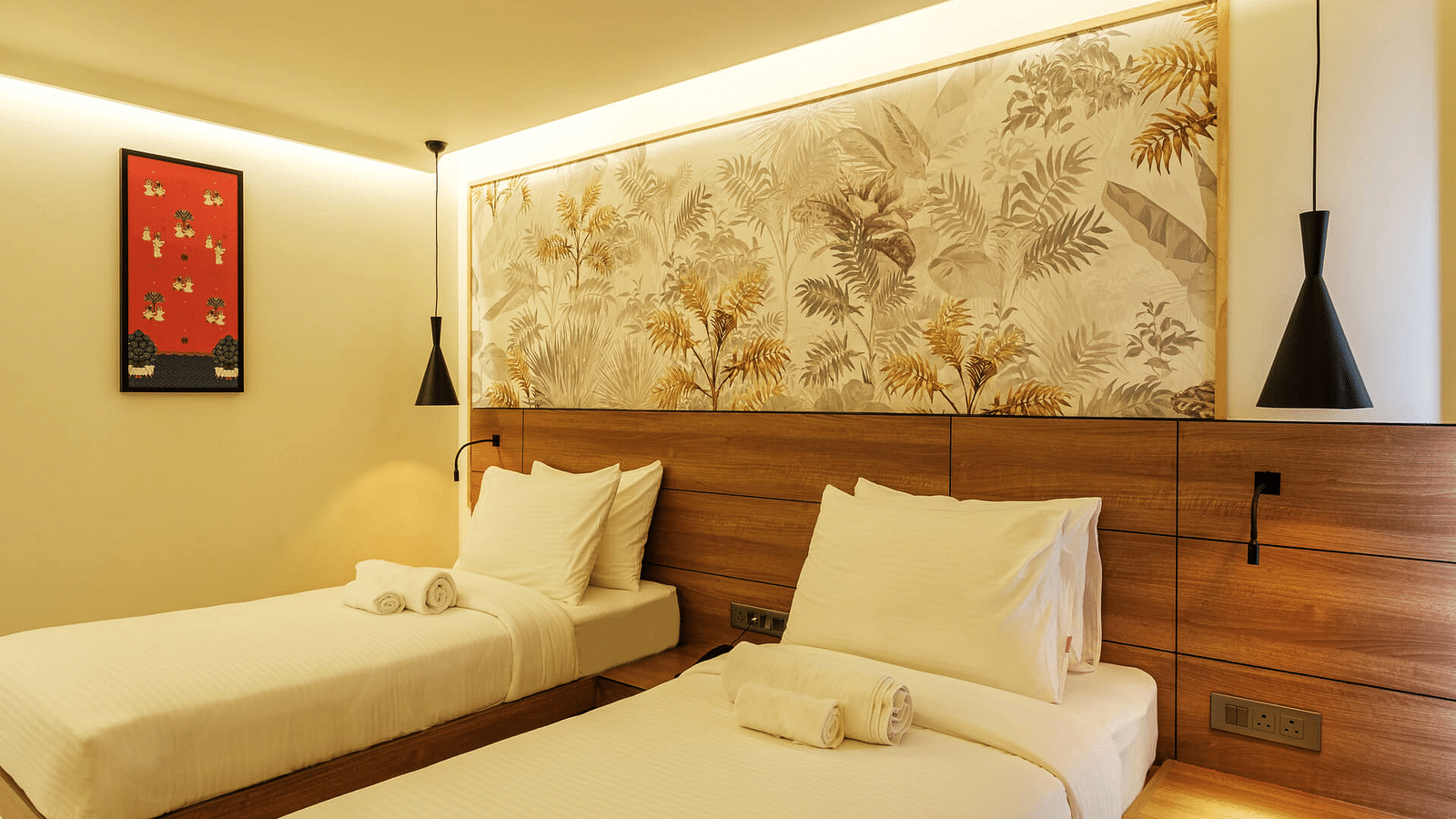 A side view of a spacious room at Indie Stays, Jaipur, with two single beds and wooden headboards.