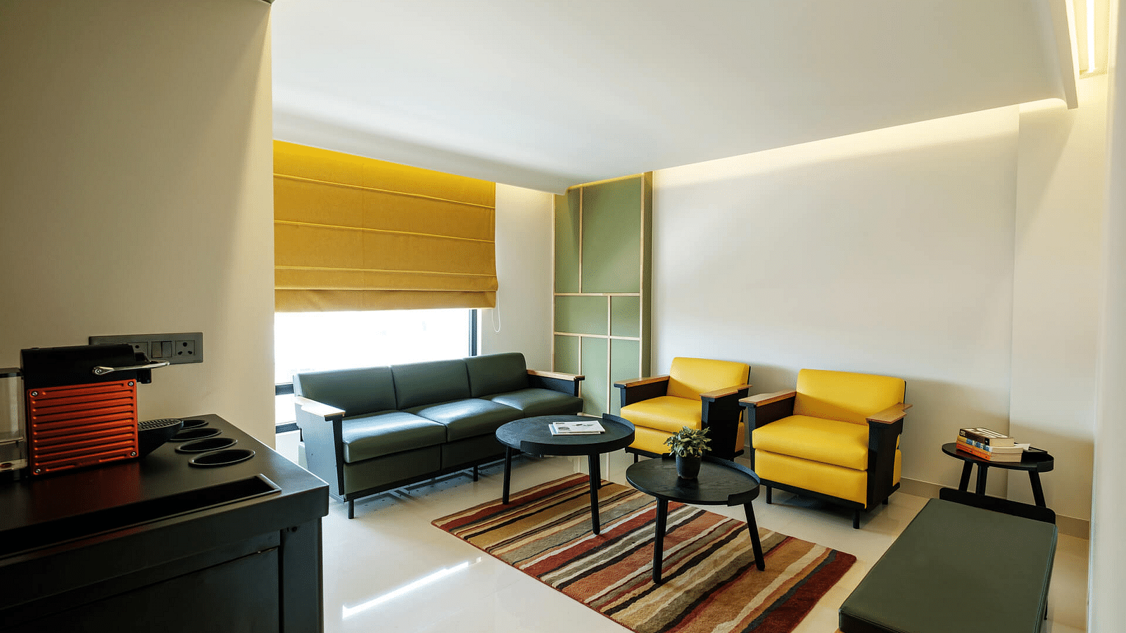 Large cushioned sofas and two round coffee tables placed in the centre, above a floor mat, with curtains pulled halfway down and a small storage unit to the side at Indie Stays, Jaipur.