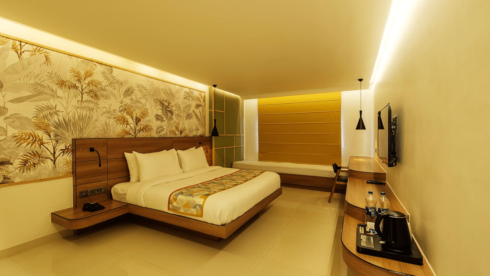 A spacious room at Indie Stays, Jaipur, featuring a large bed with a wooden headboard, a wall-mounted TV with a wooden shelf below, and curtained windows.