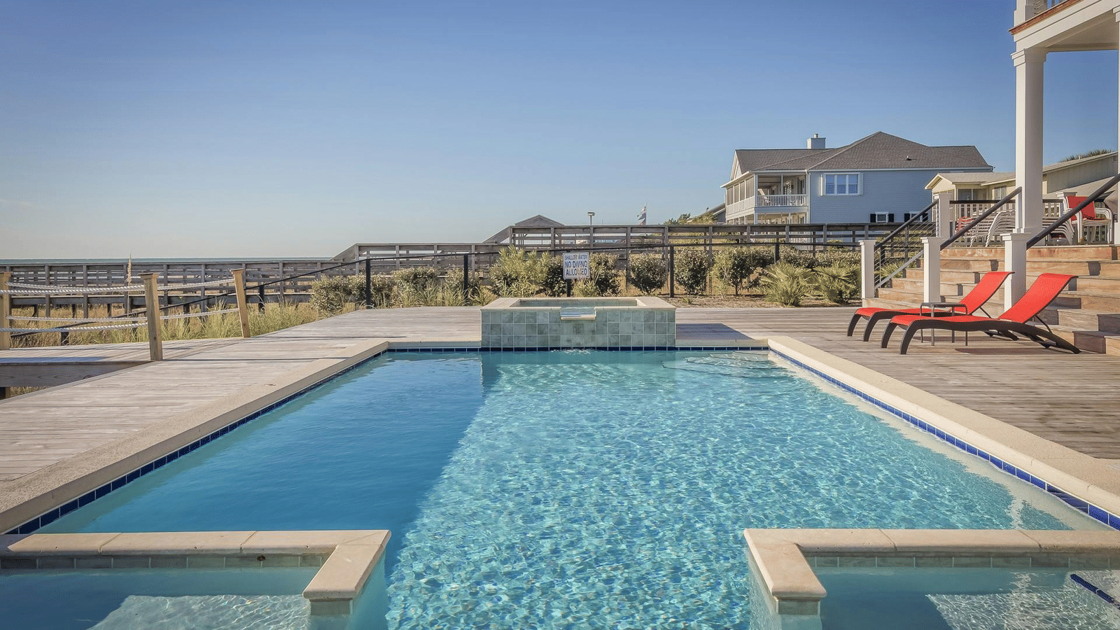 Modern outdoor swimming pool with lounge chairs and a clear blue sky in a serene residential setting.