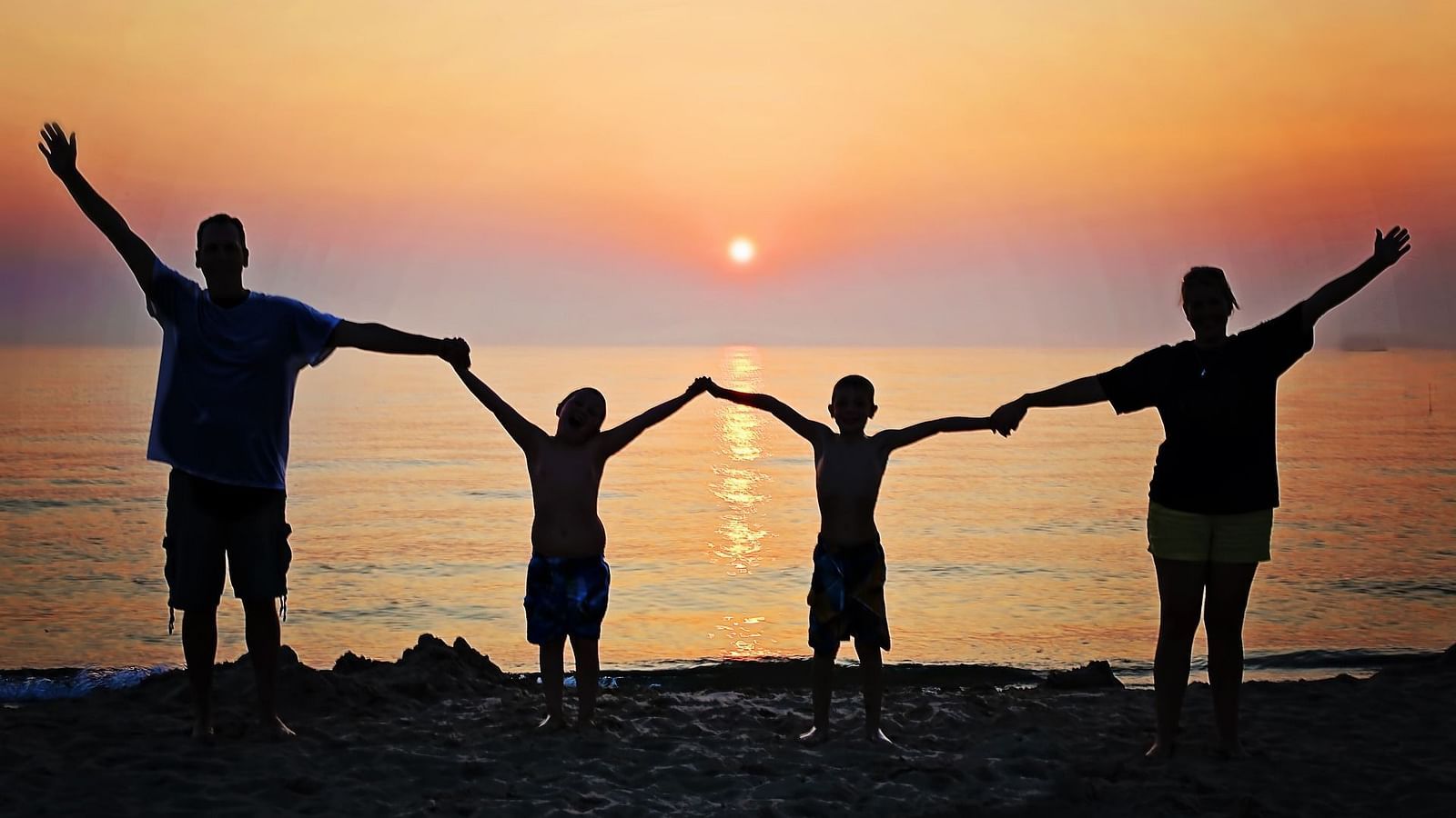 a family of four holding hands in front of a beach and sun setting in the background