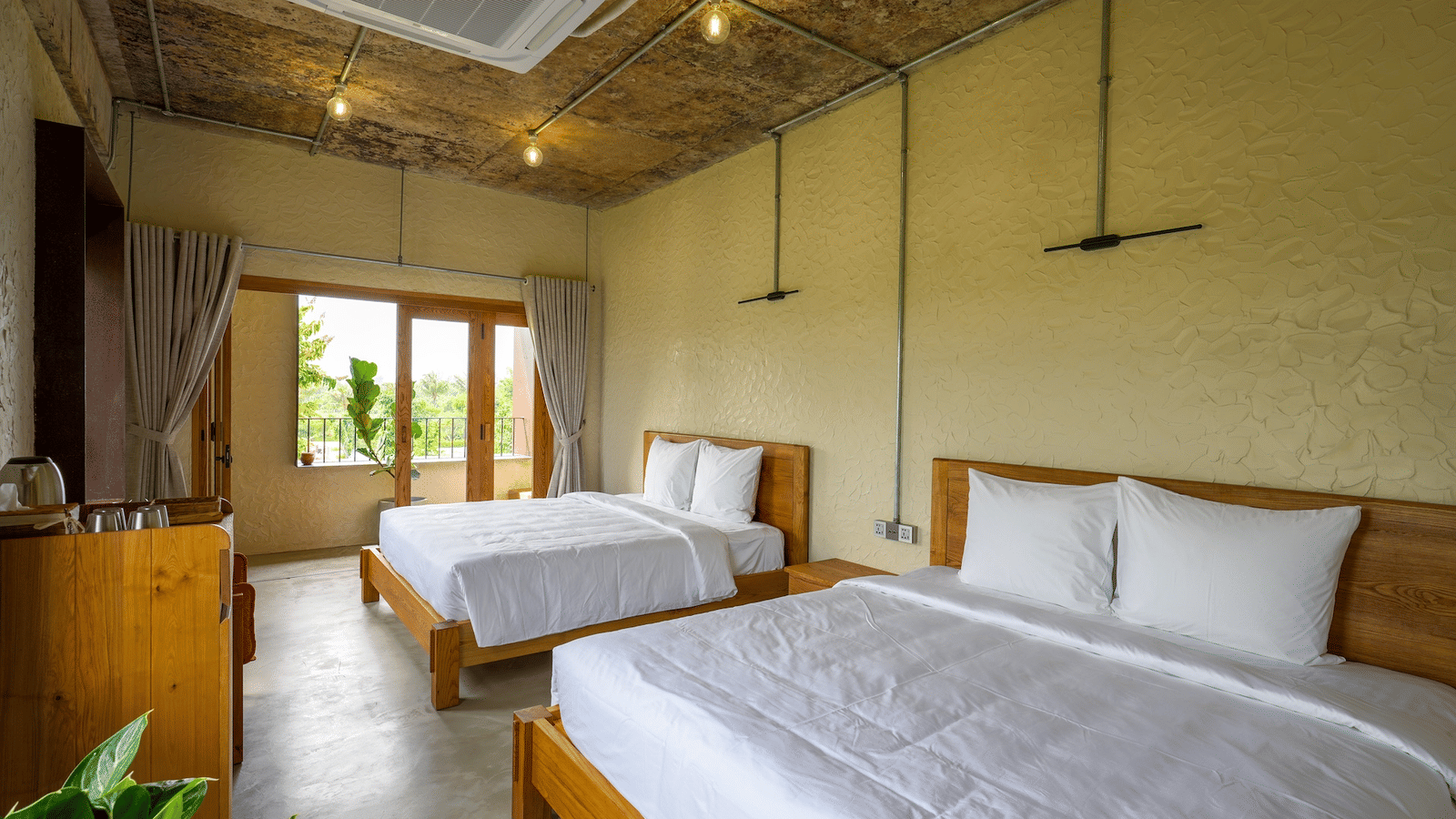 A room in WoCAL Retreat Ke Ga featuring two neatly made double beds with white linen and a window streaming natural light through.