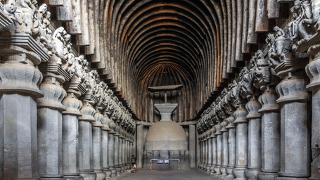 Interior of the ancient rock-cut chaitya hall at Karla Caves in Lonavala with carved pillars and a central stupa.