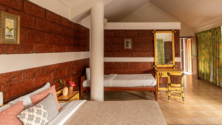 A double bed room, another single bed, a pillar, side table, wooden floor and a mirror