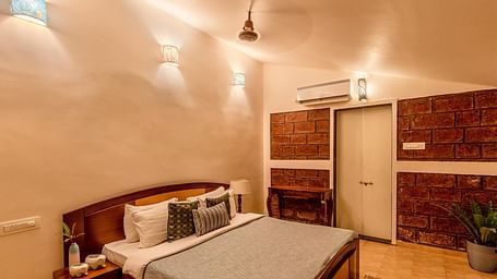 A double bed room with a side table with amenities, lights, ceiling fan, wooden floor and door