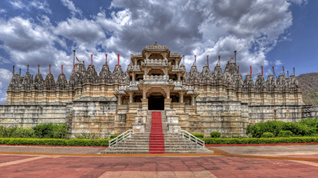 A wide shot of Ranakpur Jain Temple with a pathway leading to its grand entrance under a cloudy sky.