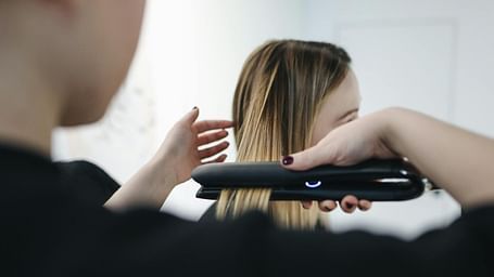 A woman sitting while another person straightens her hair with a hair straightener