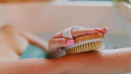 A person gently exfoliating their hand with a body brush.