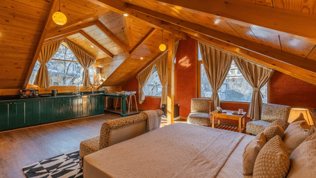 Elevated view of a luxury attic master suite with vaulted wooden ceilings, a king-size bed, and cosy seating area - Johnson Lodge & Spa, Manali