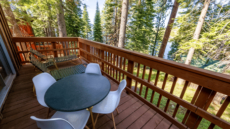 An outdoor deck at Kit Carson Lodge featuring a round dining table with chairs surrounded by tall trees and scenic lake views