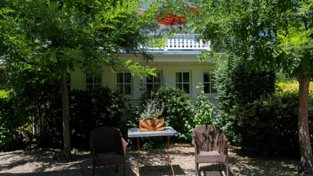 A view of garden seating area at Tallman Hotel with chairs and tables under the trees with a small white cottage in the back