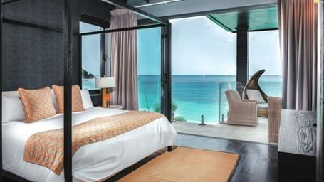 A double bed beside a floor to ceiling sliding glass door leading to a private beach.