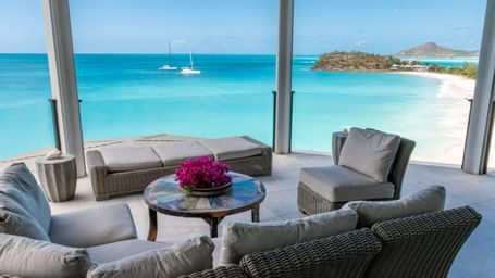  Balcony lounge area overlooking a pristine tropical beach with calm waters and distant sailboats.