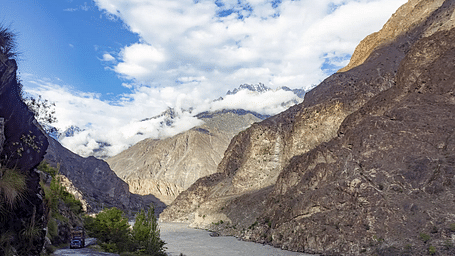 A river flowing in the foothills of a mountain with a narrow road right beside it.