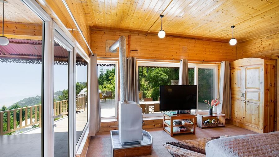 An image of room with a bed, tv screen, wardrobe, tables, and cabinet with a backdrop of balcony view