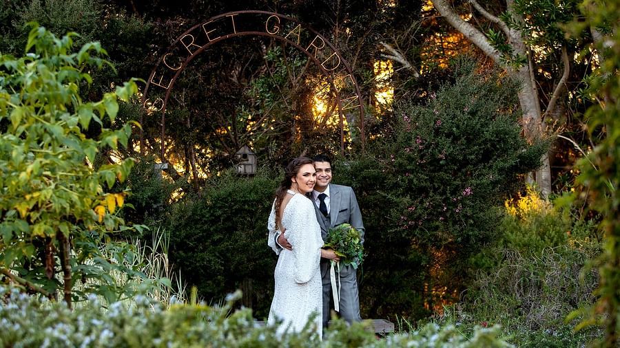 Newlyweds posing in a lush green garden under an enchanting archway