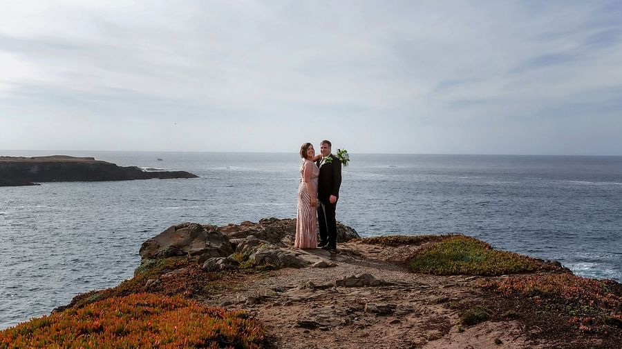 Bride and groom embracing on a rocky cliff with the vast ocean behind them