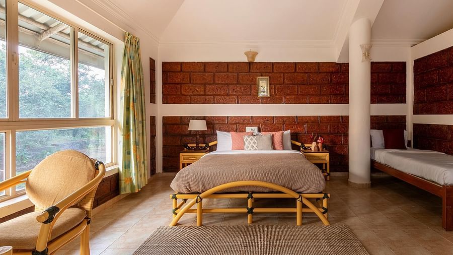 A double bed room with rug, glass windows with curtains, wooden floor, pillar, work chair and side tables