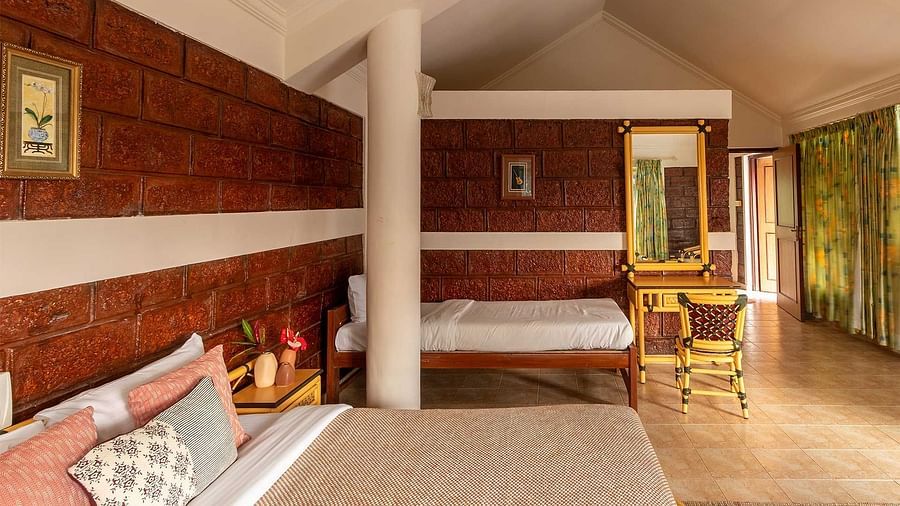 A double bed room, another single bed, a pillar, side table, wooden floor and a mirror