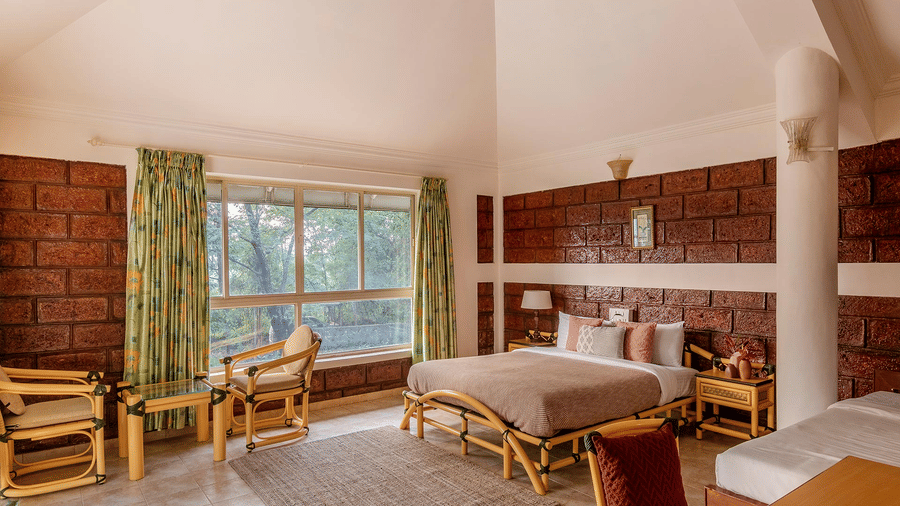 A double bed room with a side table, wooden floor, rug, pillar, chairs, table and windows with curtains at Conservancy Bungalow