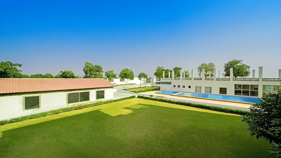 An elevated view of the building showing a lawn, some low-rise buildings, an outdoor swimming pool, and a clear sky at Grassfield Riveria Resort.