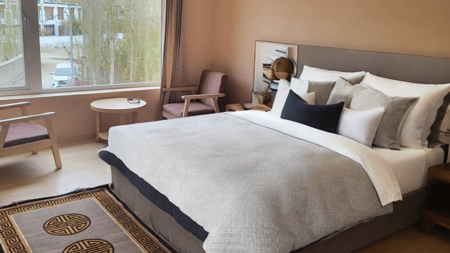 A bright Premium Room at Hotel Dekiling by Eastlynn Collections, Leh, featuring a double bed, seating area by the window, and a traditional rug.