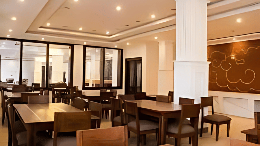 An indoor restaurant area at Hotel Dekiling by Eastlynn Collections, Leh featuring dark wooden tables and chairs set under warm recessed lighting.
