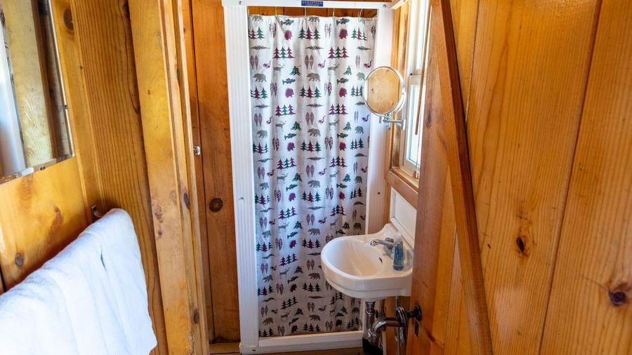 Small bathroom with wood paneling, shower curtain, and sink in a simple cabin at Kit Carson Lodge.