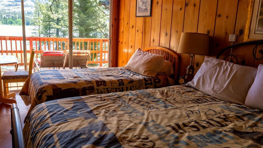 Twin beds in a warm wood-paneled room with forest views through wide windows at Kit Carson Lodge.