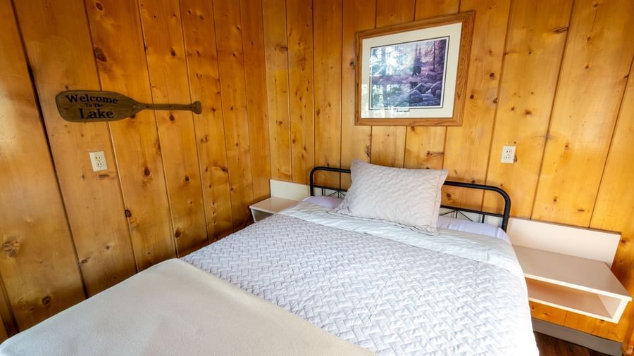 Bright bedroom with white bedding, wooden decor, and art on the wall in a peaceful cabin at Kit Carson Lodge.