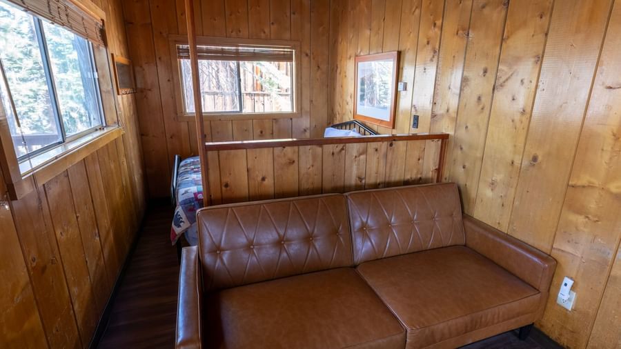 Compact sitting area with leather loveseat and wood-paneled walls in a quiet cabin at Kit Carson Lodge.