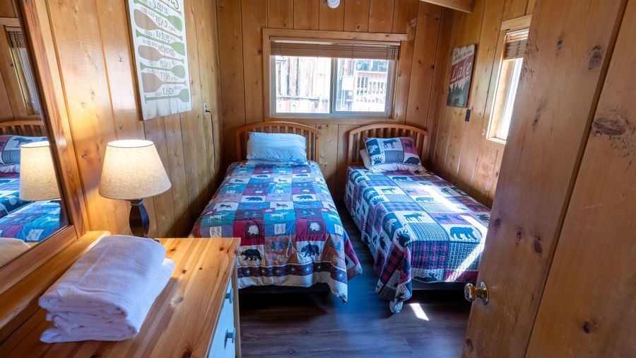 Twin beds with colorful bedding and forest views in a sunlit room at Kit Carson Lodge.