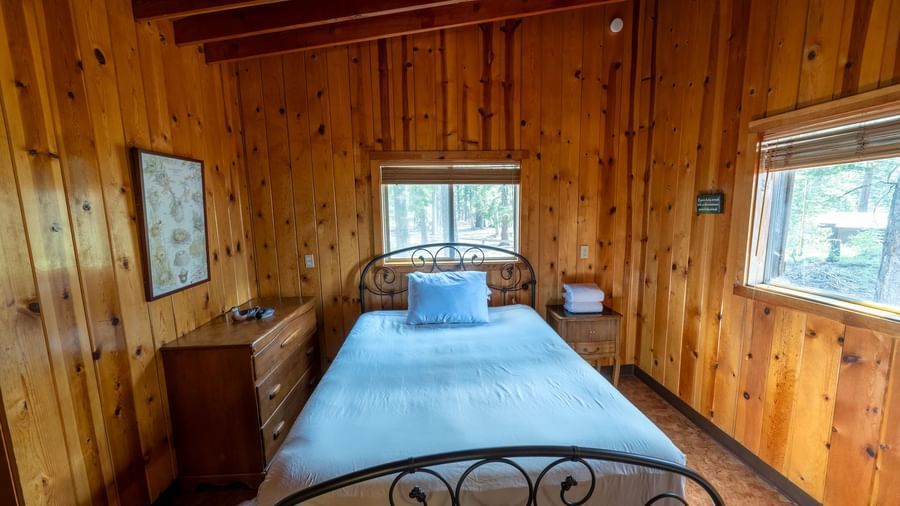 Bedroom with metal-frame bed, wood-paneled walls, and natural lighting inside a cabin at Kit Carson Lodge.