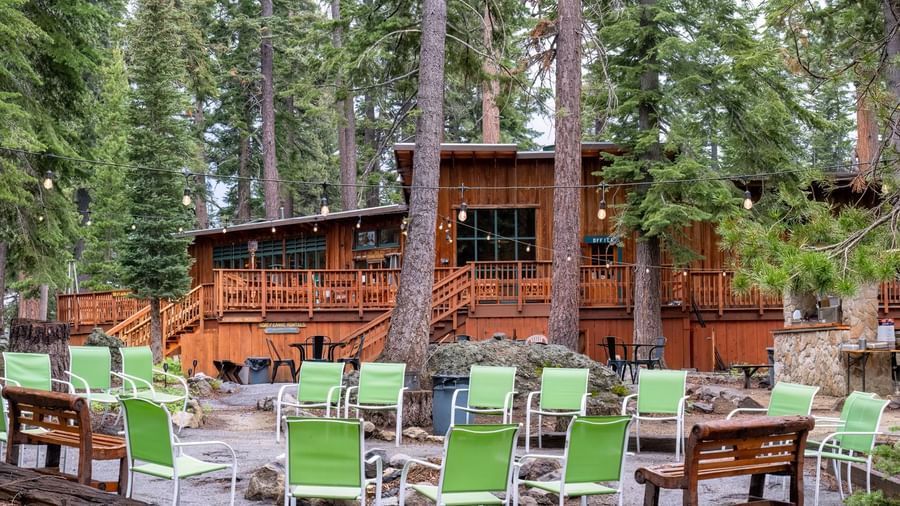 Forest patio area with green chairs and wooden deck at Kit Carson Lodge.