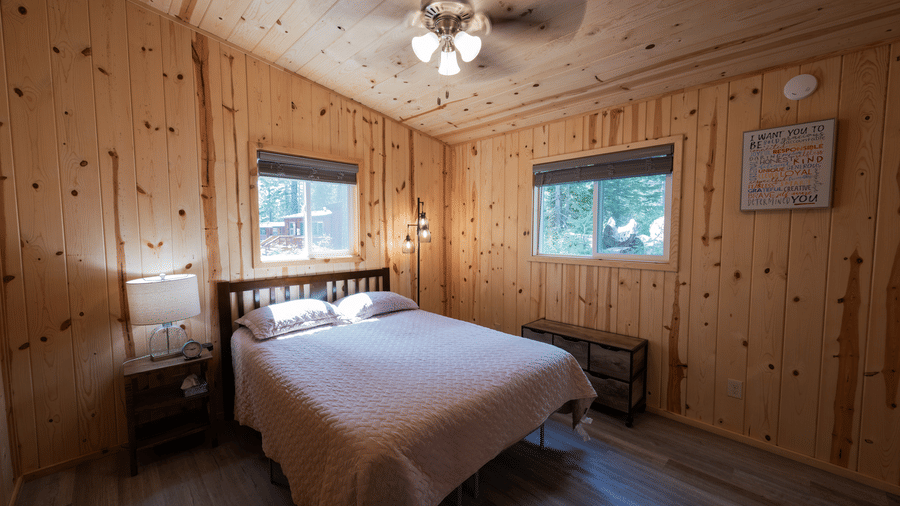 A cosy bedroom at Kit Carson Lodge featuring a comfortable bed, wooden walls, and large windows allowing natural light to fill the room