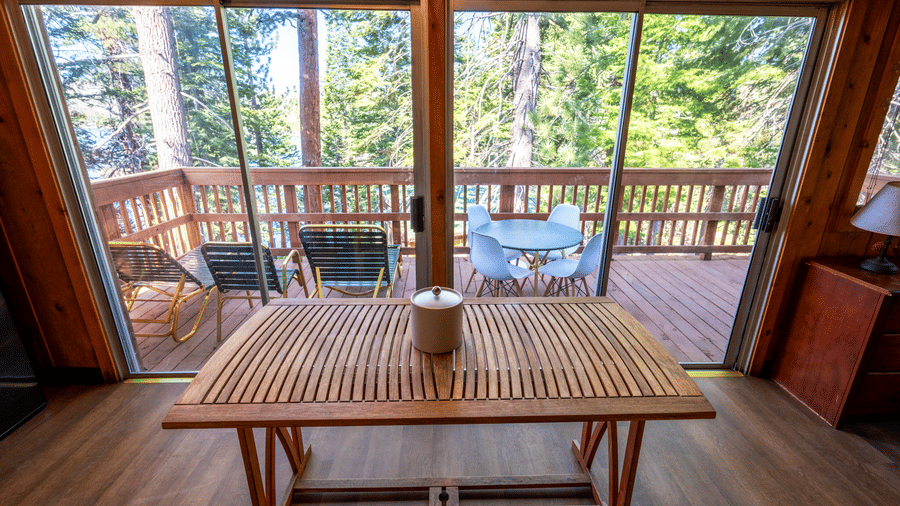 An indoor dining area at Kit Carson Lodge with a wooden table positioned beside large glass doors that open to a deck overlooking the forest